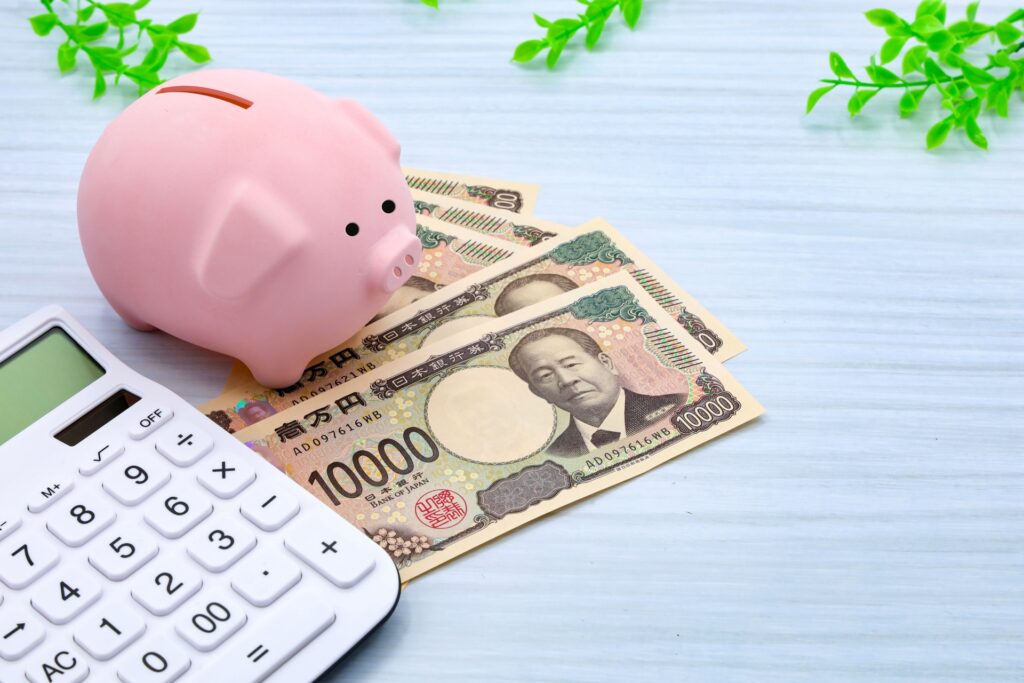電卓、貯金箱、1万円札が並ぶ節約・資産管理の写真
