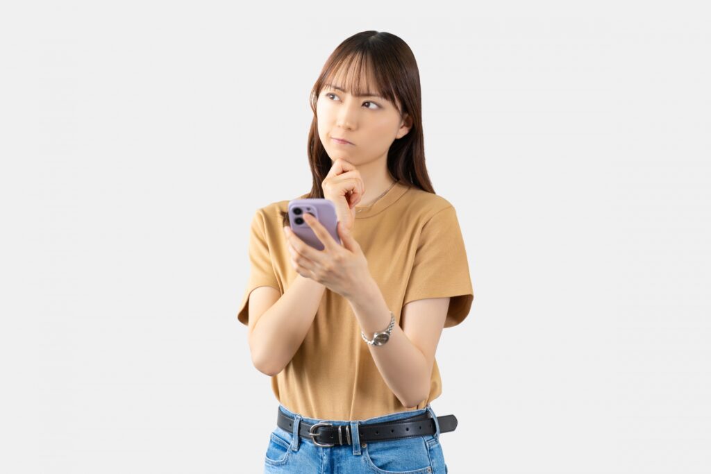 スマホを持ちながら悩む女性の画像