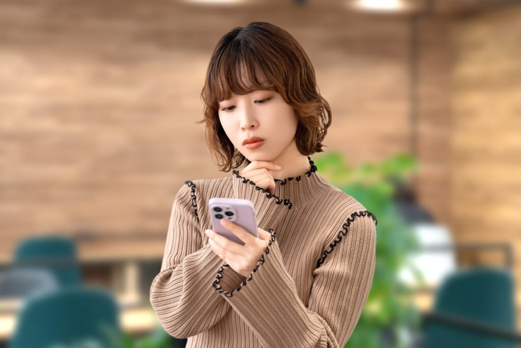 スマホを見て考える女性・ビジネスウーマンの画像