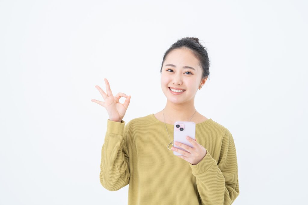スマホを持ってOKする若い女性の画像