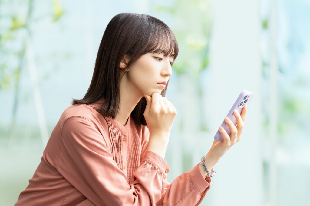 スマホを持ち悩んだ様子の女性の画像