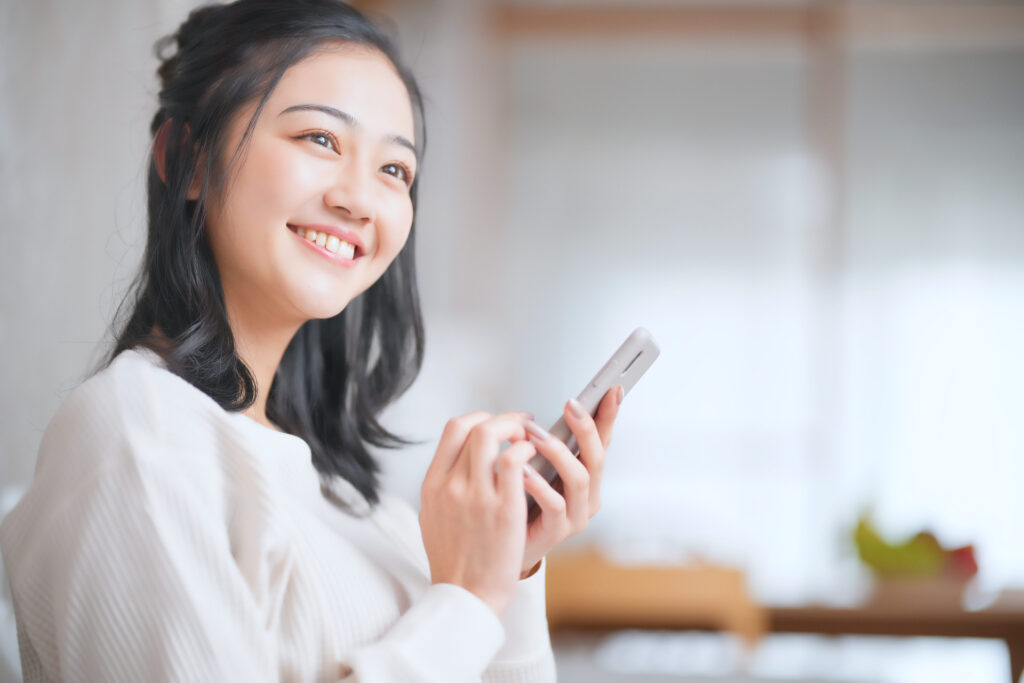 スマホを持ち笑顔で見つめる女性の画像