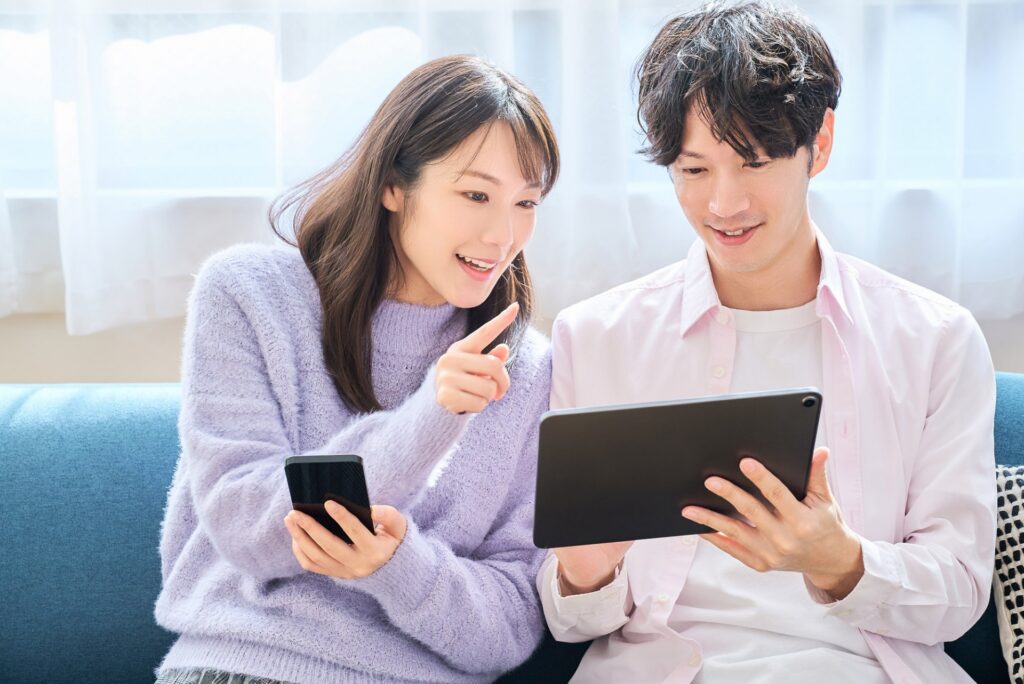 スマホとタブレットの画面を見比べる男女の画像