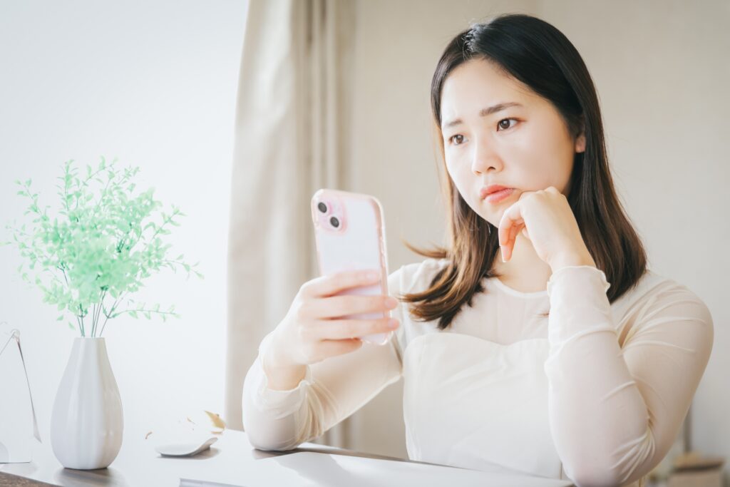 スマホを持って悩む女性の画像