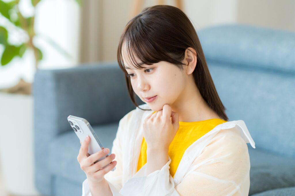 スマホを見て考える若い女性の画像